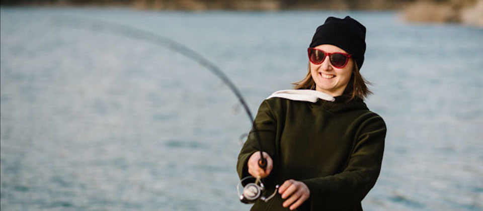 Fisherman with rod, spinning reel on the river bank. Fishing for pike, perch, carp. Woman catching a fish, pulling rod while fishing at the weekend. Girl fishing on lake, pond