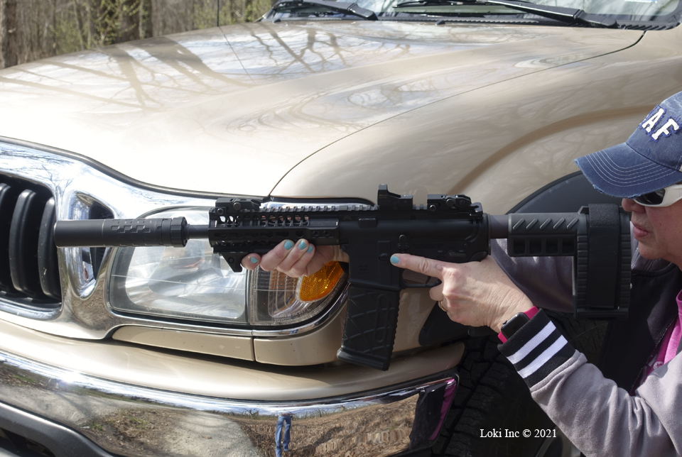 Barb with AR pistol suppressed kneeling against truck front quarter panel Saker 556 ASR