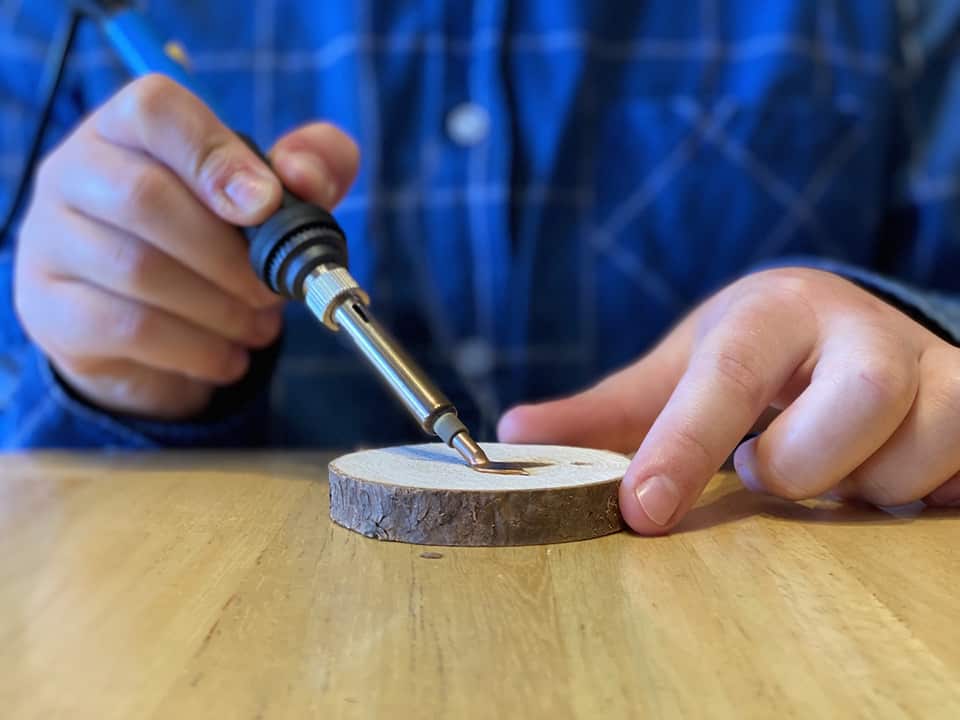 Anna uses the burning tool on her wood cookie ornament