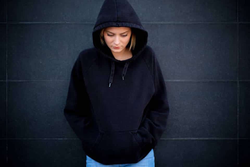 Portrait of young hooded girl on black background wall safety