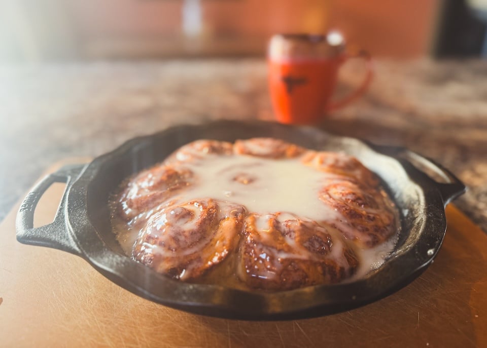 Cinnamon rolls in cast iron next to cup of coffee