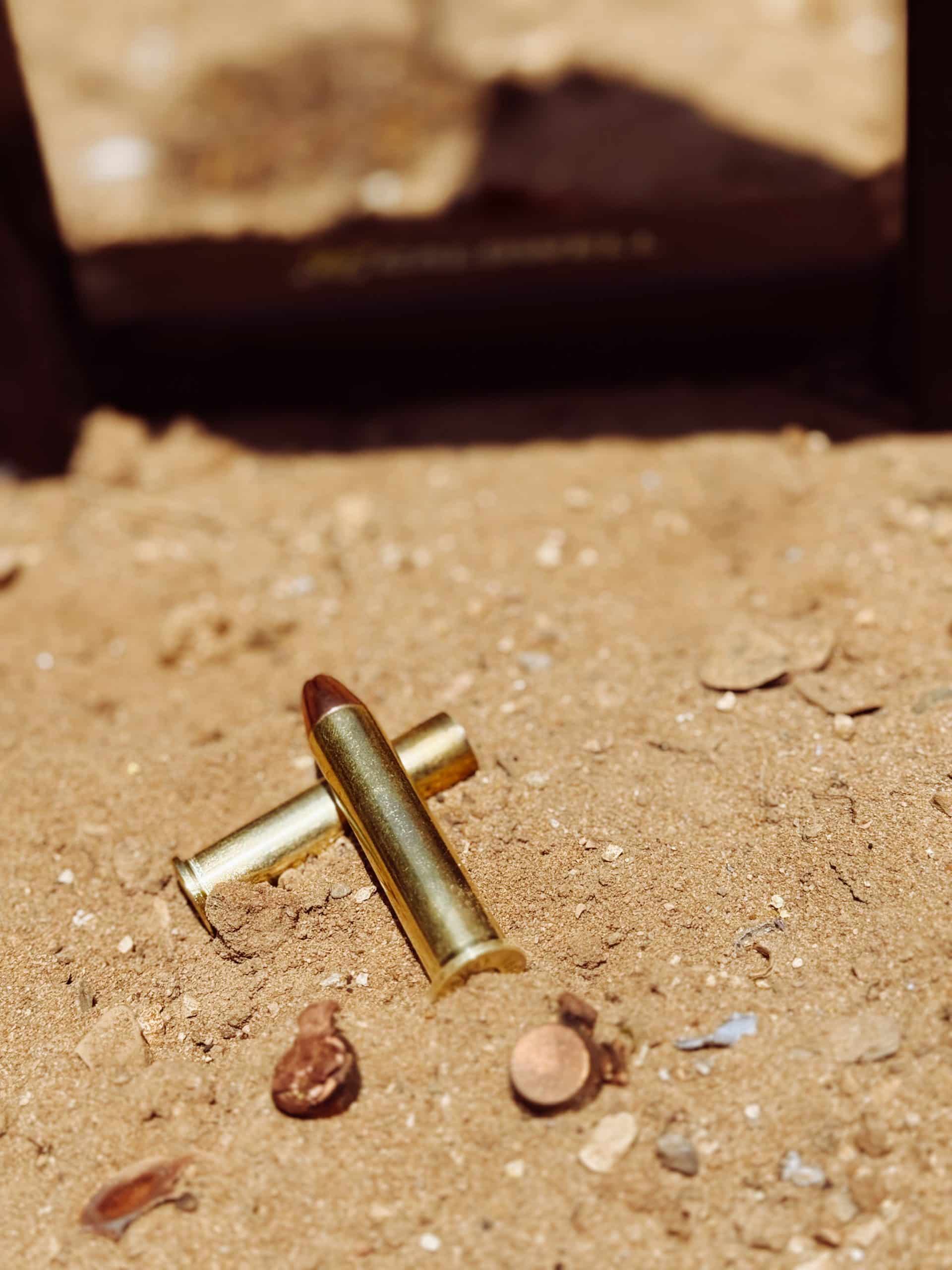 Expanded bullet and empty casing in sand next to unshot round