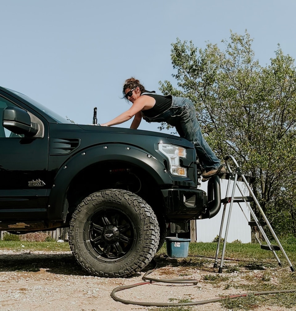 A woman washing her truck with the help of a step stool copy